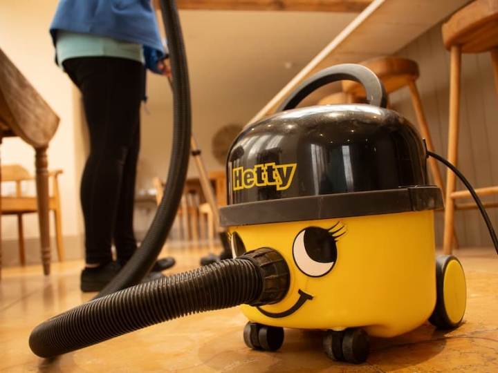 A professional cleaner using a yellow vacuum in a kitchen, ensuring a thorough and spotless clean for your home.